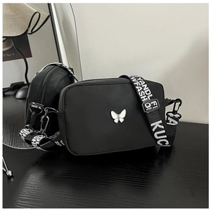 Detail of black nylon crossbody bags with wide letter straps and butterfly ornament