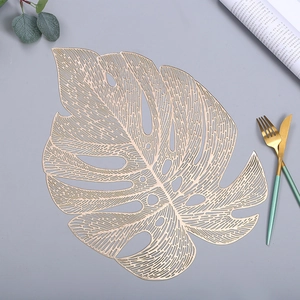 Detail shot of golden PVC monstera leaf placemat with hollow design on dining table