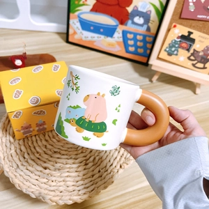 Close-up of cute ceramic capybara mug with orange handle and matching gift box