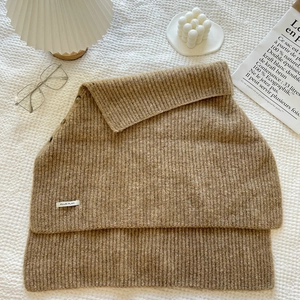 Detail of a brown ribbed knit scarf with decorative buttons and a small white brand label