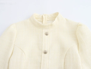 Detail van beige tweed jasje met opstaande kraag, pofmouwen en gouden metalen knopen