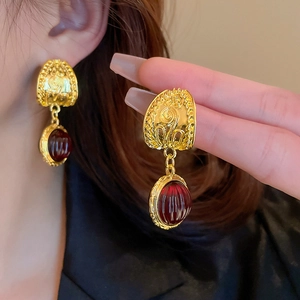Close-up of vintage gold earrings with textured deep red oval gemstones on a model