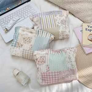 Three quilted floral cosmetic bags in pastel colors shown on a soft white bed sheet
