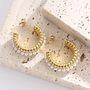 Detailed close-up of C-shaped gold-plated twist earrings with white pearls on stone