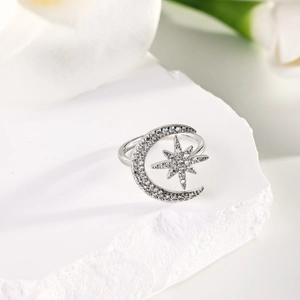 Detailed macro of a silver crescent moon and star ring on a white stone background