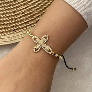 Detailed close-up of 18K gold cross bracelet with sparkling zircon stones and adjustable cord