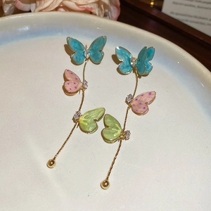 Macro detail of long butterfly tassel earrings with colorful enamel and golden chains