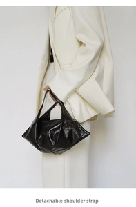 Detail of black glossy triangle bag with detachable shoulder strap worn with white suit
