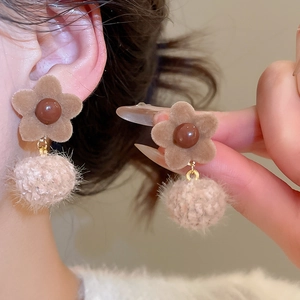 Detail view of brown flocked flower earrings with beige pom poms and warm pearl accents