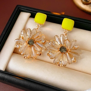 Makroaufnahme quadratischer gelber Kristallohrringe mit Blumendesign in einer Schmuckschatulle