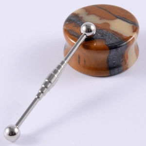 Macro detail of a polished stainless steel industrial barbell piercing on a marble stone
