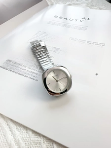Close-up of silver steel watch with square dial on white magazine and knit background