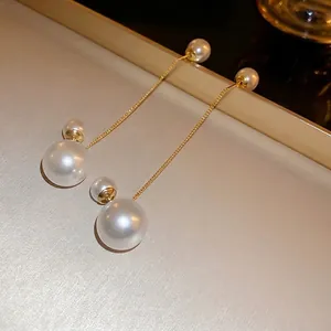 Elegant gold plated pearl tassel earrings with fine metal chains on silk background