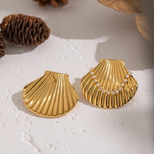 Detail view of gold shell earrings with inlaid diamonds on a white stone pedestal