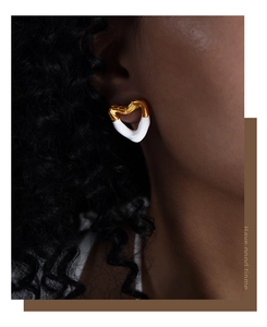 Close-up of a model wearing a heart-shaped gold and white enamel stud earring