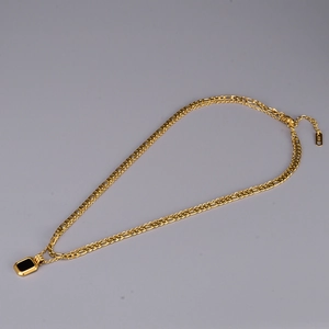 Close-up of golden Figaro chain with a black rectangular pendant and K18 engraving