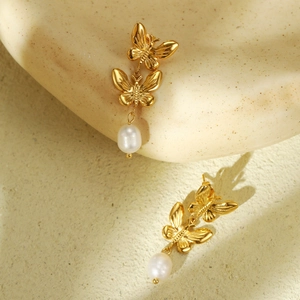 Golden butterfly earrings with white pearl droplets on artistic stone background