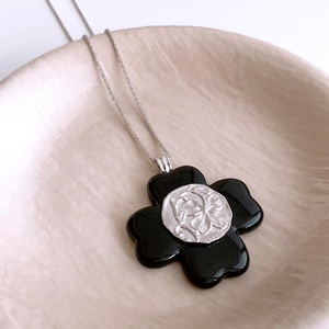 Macro detail of a resin clover pendant with silver embossed flower on a silver chain
