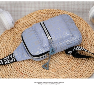 Detail view of the silver letter print and double-zipper design on the purple chest bag