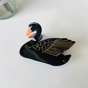 Detailed close-up of a black swan acetate hair claw clip with elegant gold feather patterns