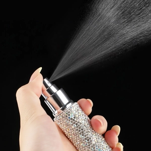 Macro shot of a hand pressing a diamond-studded spray bottle releasing a fine mist