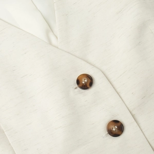 Detailed close-up of cream linen texture and dark tortoiseshell buttons on vest