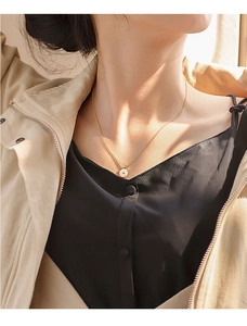 Golden coin pendant necklace with starburst detail worn on model in natural sunlight