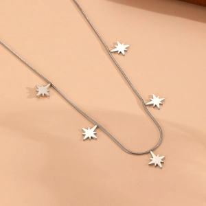 Détail d'un collier chaîne serpent argenté avec cinq pendentifs étoiles sur fond beige
