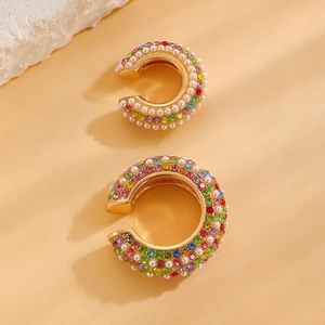 Macro detail of gold C-shape ear cuffs with colorful rhinestones and white pearls