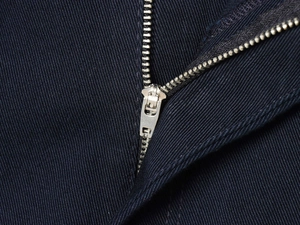 Dettaglio macro della cerniera in metallo argentato sul tessuto blu scuro dei pantaloni