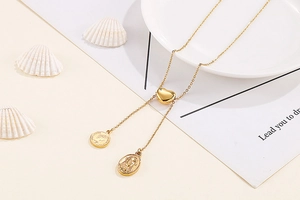 Detailed close-up of golden stainless steel lariat necklace with heart bead and coin charms