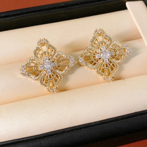 Macro shot of gold hollow flower earrings with sparkling zircons on beige velvet