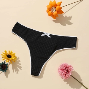 Detail of black ribbed thong with white trim and small bow on beige background