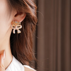Close-up of model wearing gold bow earrings with cream enamel and zircon heart drops