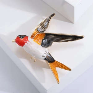 Colorful swallow bird brooch with enamel glaze and gold accents on a white pedestal