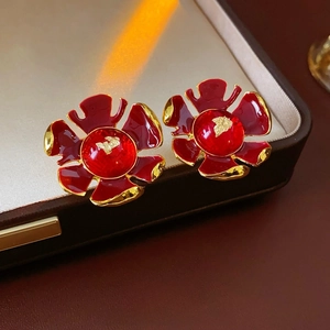 Vintage red enamel flower earrings with gold trim on brown leather tray with warm lighting