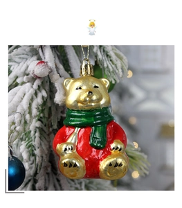 Close-up of a festive golden bear ornament with a green scarf on a snowy tree branch