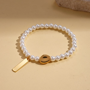 Detail of 18k gold plated OT toggle chain bracelet with pearls and charms on beige stone