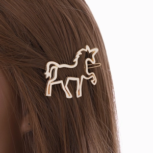 Unicorn shaped hair clip with gold metal cutout and white enamel on brown hair