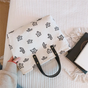 Détail du sac cabas en toile blanche avec imprimé floral noir et poignées en cuir sur fond blanc
