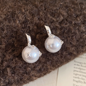 Macro shot of silver C-shaped pearl earrings with star-shaped zircons and matte finish