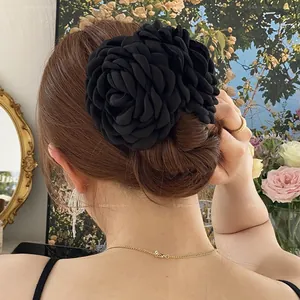Dettaglio di una grande molletta a rosa in tessuto nero indossata per uno chignon elegante