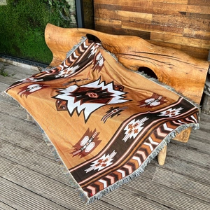 Detailed view of bohemian woven blanket with Aztec patterns and fringe on a wooden bench