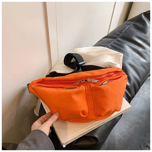 Detail of an orange nylon crossbody bag with dual front pockets and adjustable strap
