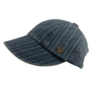Detail view of denim baseball cap showing bronze metal badge and woven fabric texture
