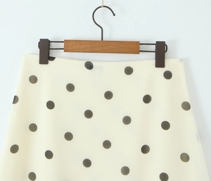 Detailed view of polka dot skirt waistband on a wooden hanger with cream fabric texture