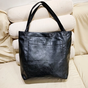 Détail du sac cabas vintage en cuir noir avec grande capacité et poche avant sur canapé