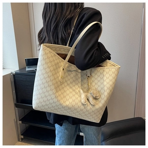 Close-up of large tote bag with monogram pattern and cute puppy charm on a model