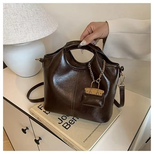 Detailed view of deep brown oil wax leather handbag with mini charm on a white cabinet
