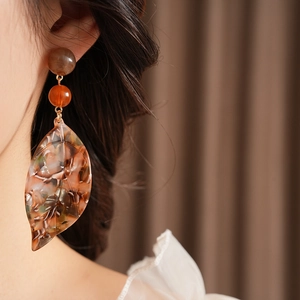 Close-up of amber acetate leaf earrings worn by a model in soft lighting